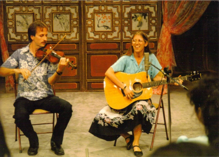a woman sitting next to a man while playing the guitar