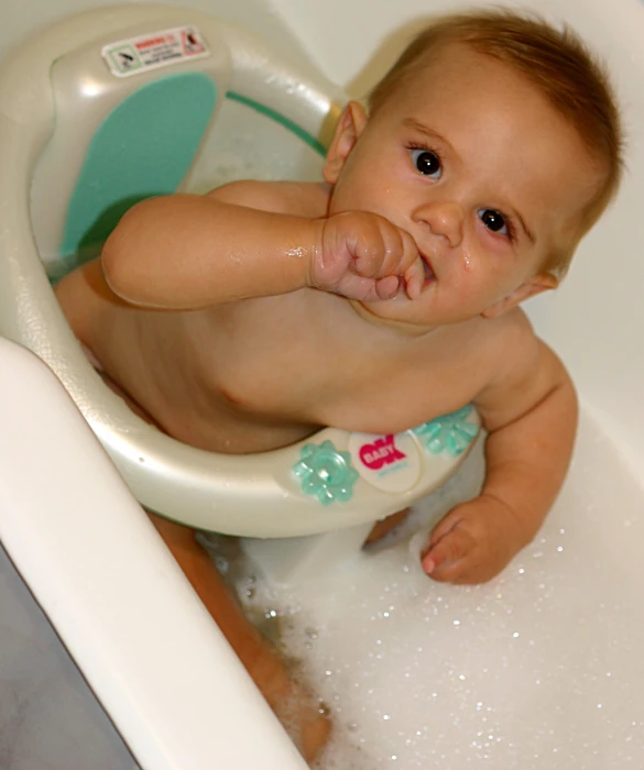 an infant plays in a bathtub with a large toothbrush