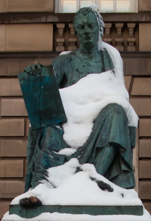 a statue holding a book sits in the snow