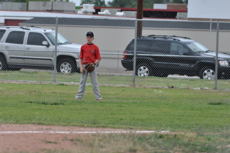 a young man wearing a red baseball jersey standing on a field with a mitt in hand