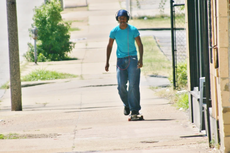 a man in jeans and a t - shirt riding a skateboard down a sidewalk