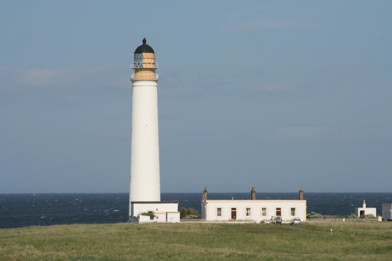 a light house on a grassy hill with the ocean in the background