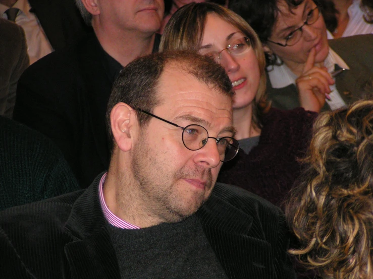 a man in glasses sitting next to a crowd of people