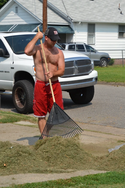 a man wearing red shorts and holding a large broom on the side of a road