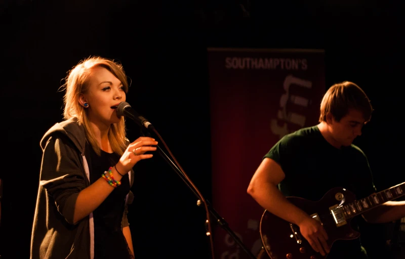 a woman holding a guitar and a man singing into a microphone