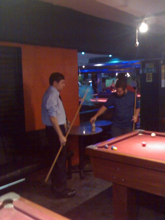 two men playing pool in a dark room