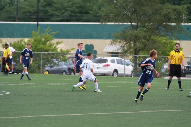 boys on a soccer field playing soccer and the referee is directing the players