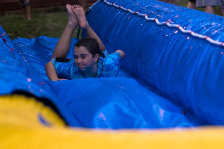 a boy sliding down a blue and yellow obstacle