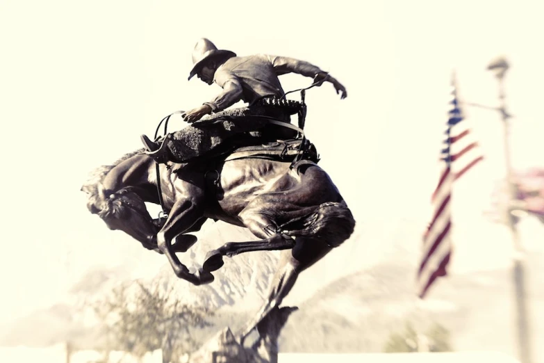 statue of a cowboy riding a bucking bronco horse next to american flags