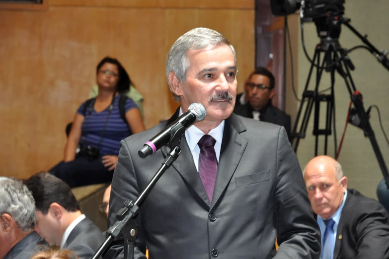 a man standing in front of a microphone with people in the background