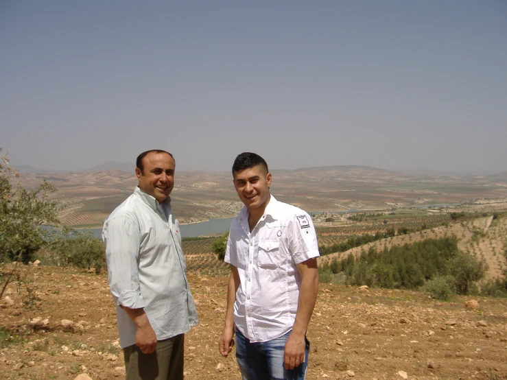 two men stand together on the side of a hillside