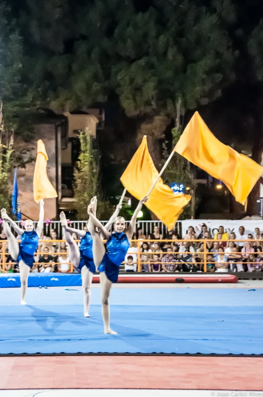 three girls in blue and yellow cheerleader outfits hold flags behind them