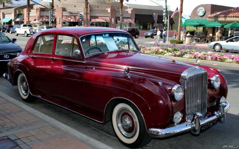 a classic car parked on the street near flowers