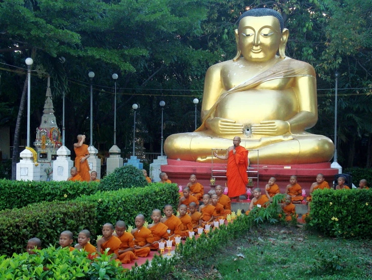 people are standing near a large golden statue in a park