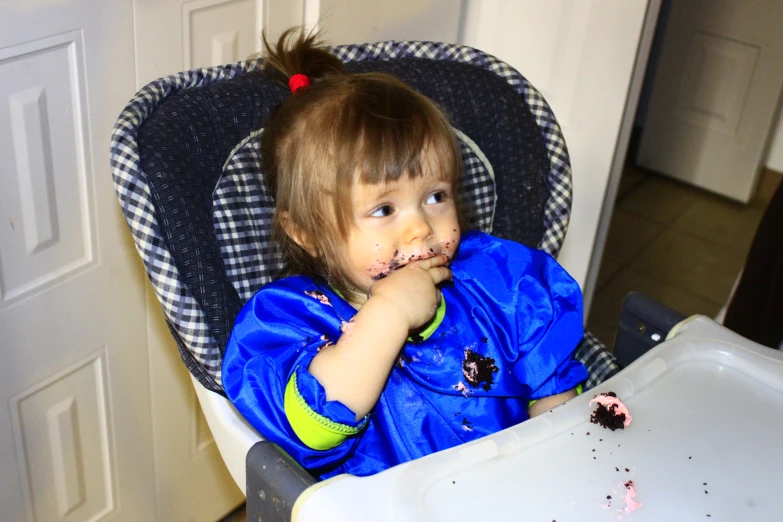 young child in blue coat eating food off of high chair