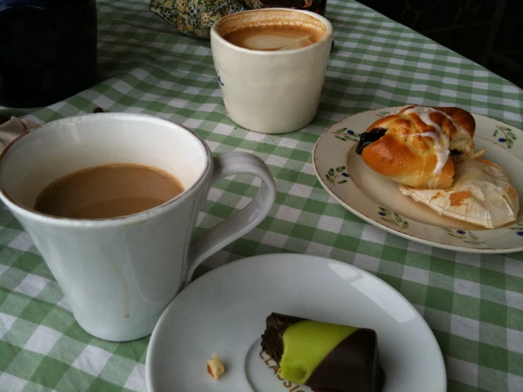 two cups of coffee are set on a table with pastries