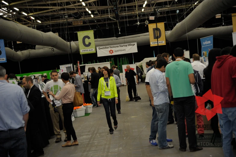 people milling around at a stand with a bright green vest