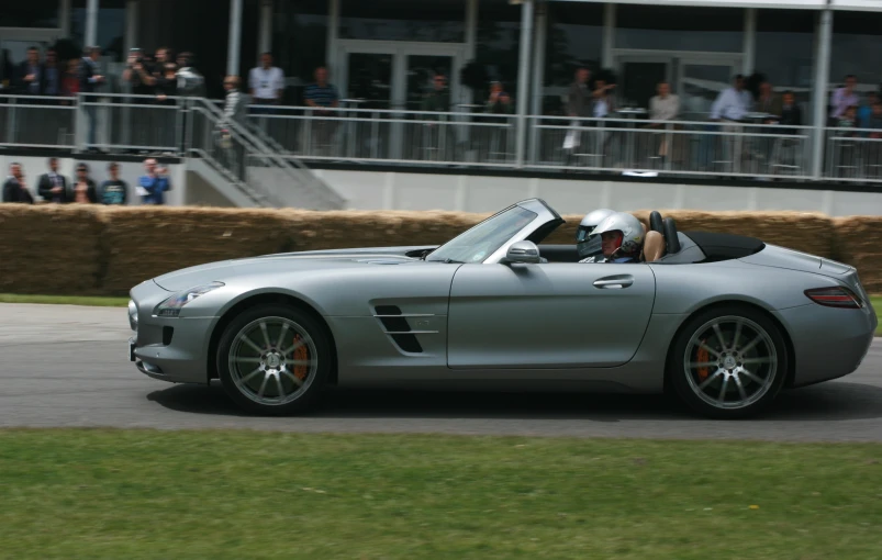 a silver sports car driving down a road while people watch