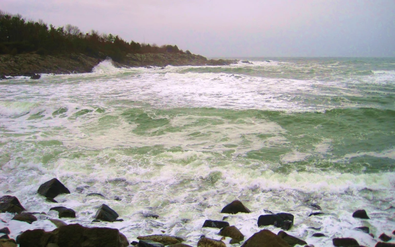 a large ocean wave hitting the shore near rocks