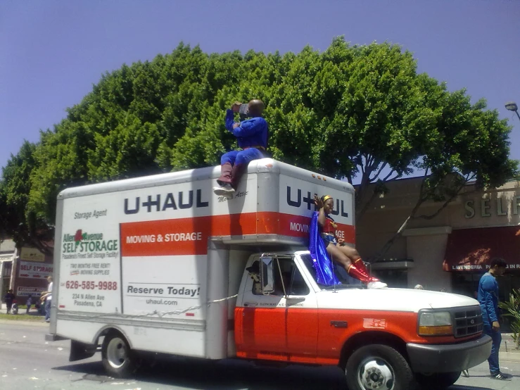 two men sitting on top of an orange and white truck