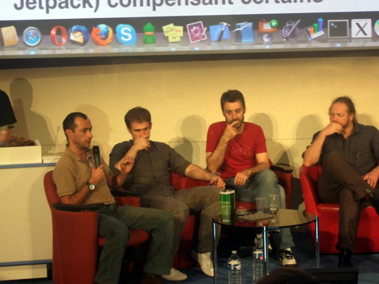 four men are sitting in red chairs talking