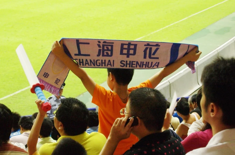 a man in orange shirt holding up sign with asian characters on it