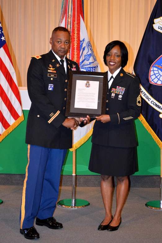 a soldier in uniform poses for a picture with a military woman in front of flags