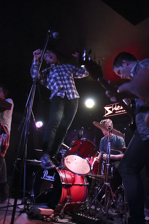 a man in plaid shirt standing on stage with drums