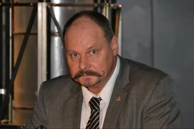 a middle aged businessman with a mustache stares straight ahead