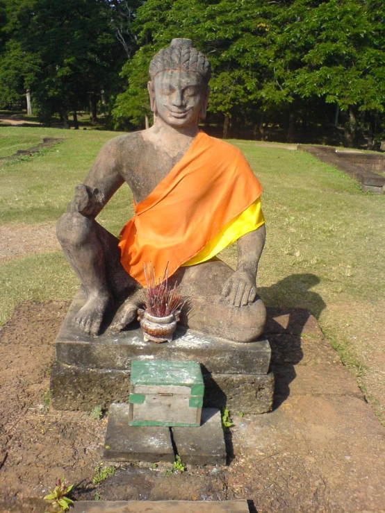 a statue with a yellow and orange cloth sitting next to a plant in the grass