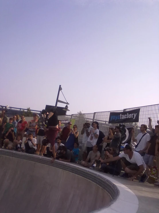 a crowd at an event looks on as a guy performs a skateboard stunt