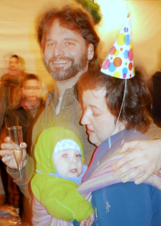 a man holds a baby while wearing a party hat