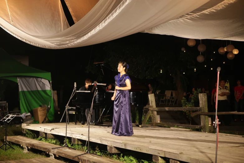 a woman is standing in front of a microphone while another person plays on a stage