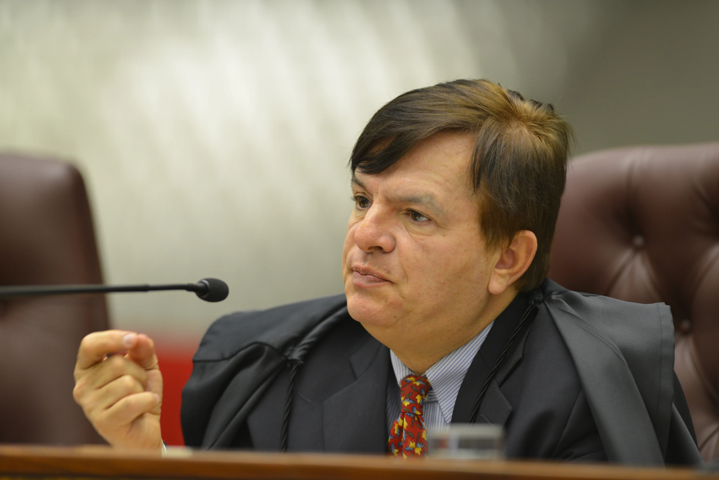 a man in business suit and tie sitting in front of a microphone