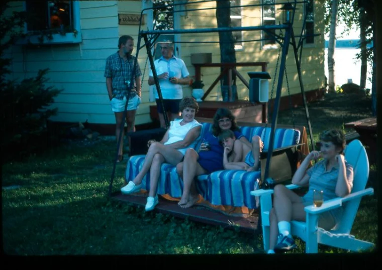 some people sitting on a wooden swing and another person standing