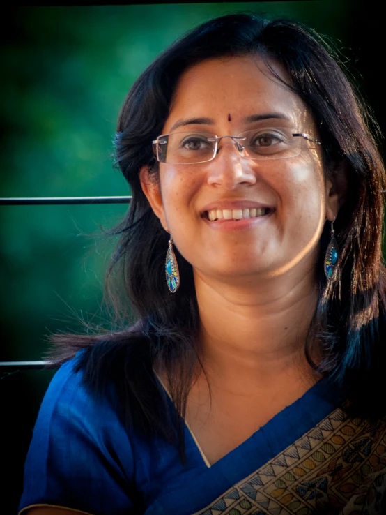 a woman smiling with glasses, blue shirt and other jewelry