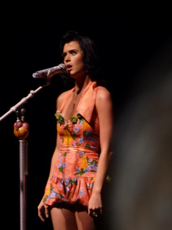 a woman in an orange dress on stage with a microphone