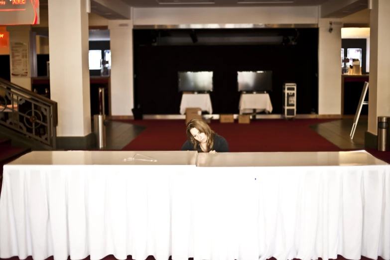 a woman is sitting at a rectangular table in a long building