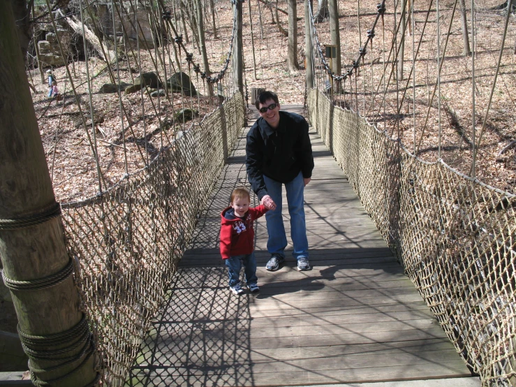 the man is walking with his toddler down the wooden bridge