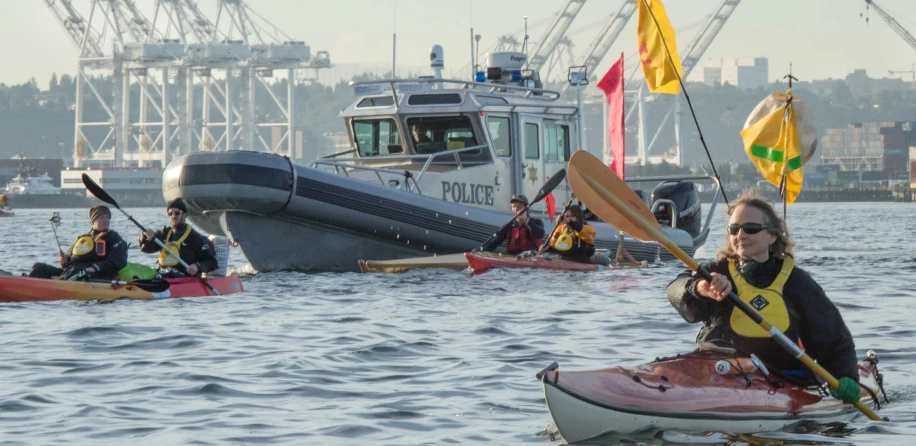 people on their kayaks in the water while another one is sitting on the bow