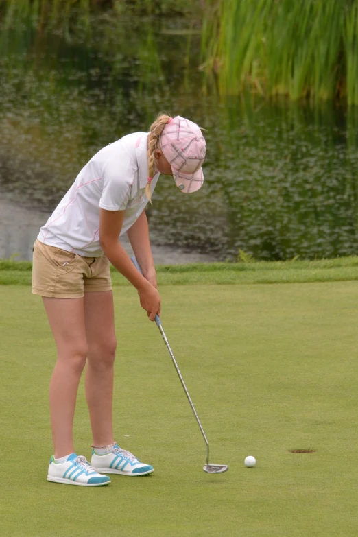 the girl is playing golf with her pink hat on