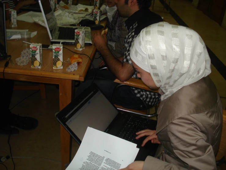 two people are sitting at a table working on laptops