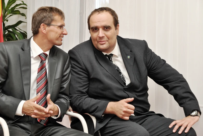 two men talking together while wearing suits and ties