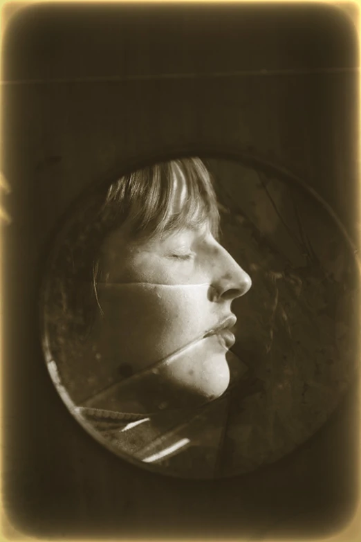 a person with their eyes closed looks into a round mirror