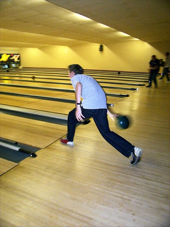 a man in an indoor bowling alley has one foot on a ball and holds the other hand out for a game