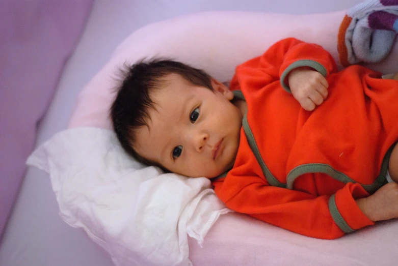 a baby in orange clothes laying on top of a pink bed