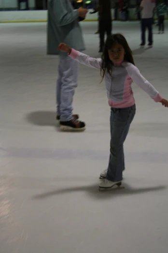a  skates on an ice rink while a man holds his arms out