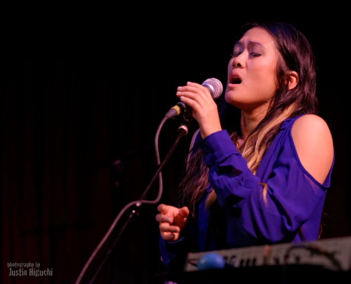 woman in purple dress holding microphone up to sing into microphone