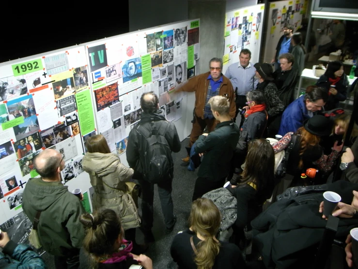 a group of people are looking at posters and listening to someone