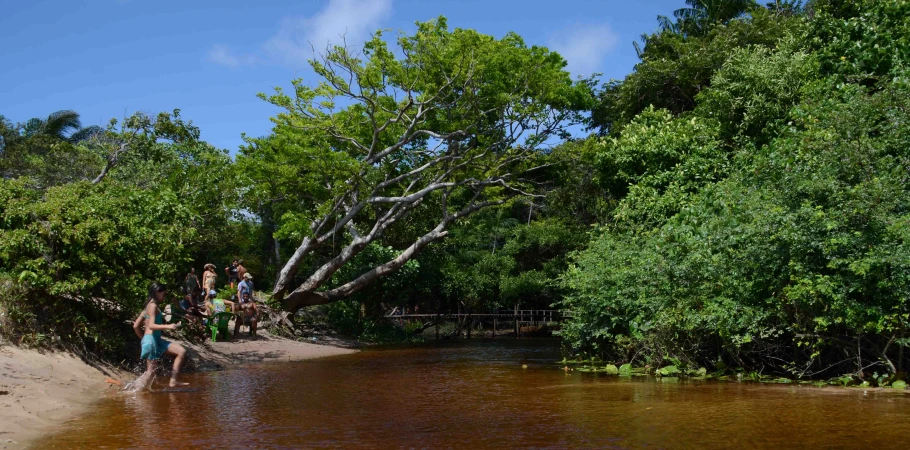 three people are playing frisbee on the shore of a river